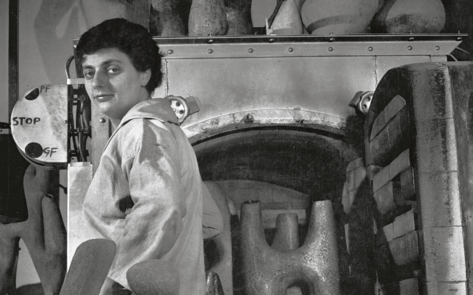 Photographie en noir & blanc représentant Valentine Schlegel dans son atelier, devant son four et entourée de sculptures.