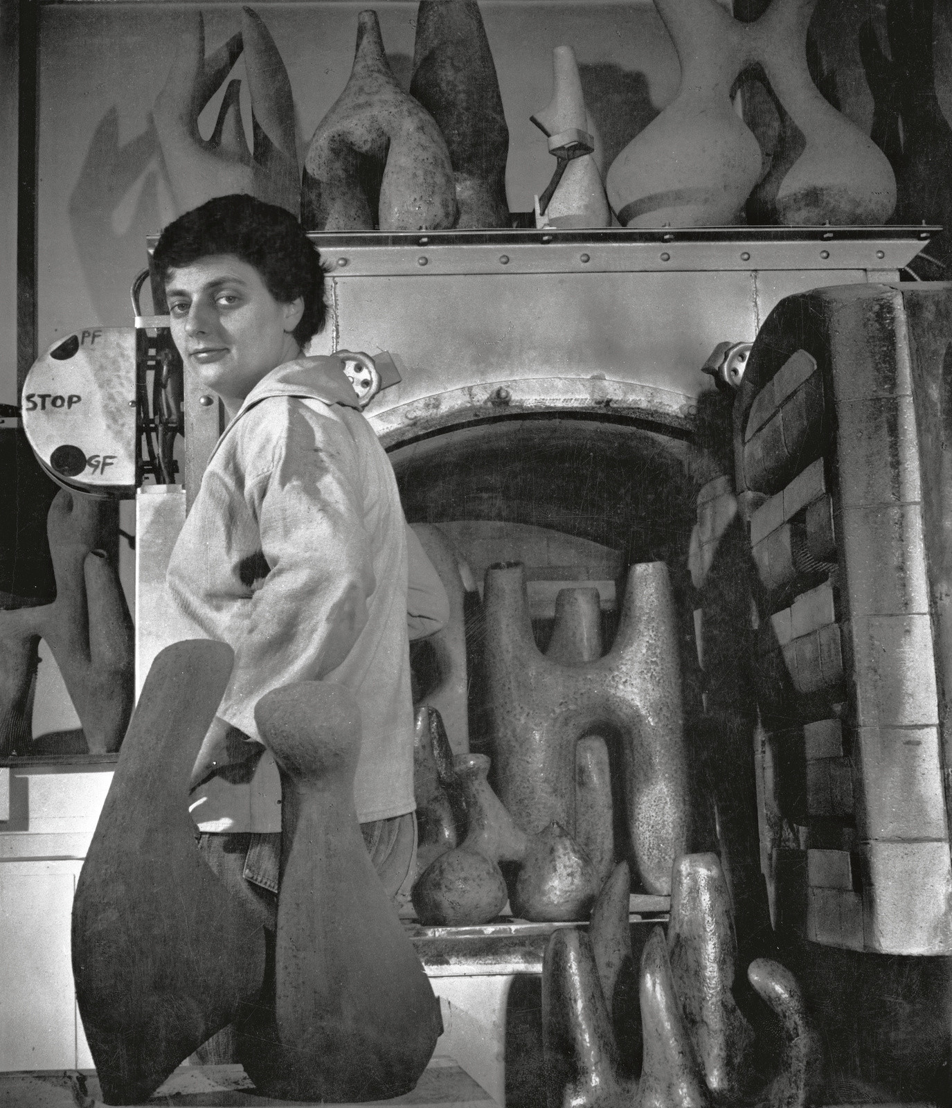 Photographie en noir & blanc représentant Valentine Schlegel dans son atelier, devant son four et entourée de sculptures.