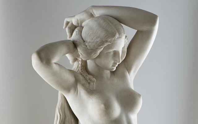 Sculpture en marbre représentant une jeune femme nue  (Nyssia, l'épouse du roi Candaule) et se tenant l'arrière des cheveux de ses deux mains.