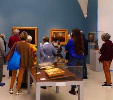 Dans une salle du musée, un groupe de visiteurs, de dos, regarde un tableau.