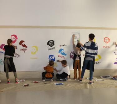 Un groupe d'enfants, dos à l'objectif, réalisent des graffitis en pochoir, représentant divers portraits de Gustave Courbet