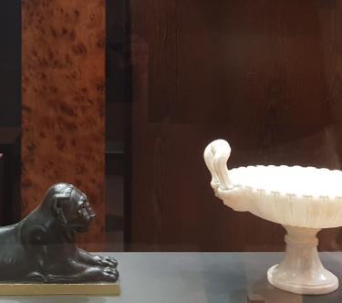 Deux objets d'art dans une vitrine : une sculpture d'animal et une coupe.